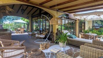 An outdoor seating area with wicker furniture, a hanging lamp, and a view of greenery.