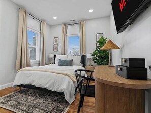 A bedroom with a bed, bedside tables, a desk, a chair, a TV, and a plant. - Modern LUX | Deck+ Parking | Near T Harvard/MIT/BU (Cambridge)