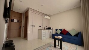 A modern living room with a blue sofa, a small side table, and a kitchen area with cabinets and a microwave. - Velmist Residence Abha (Abha)