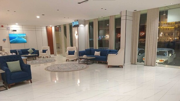 A spacious lobby with a polished marble floor, blue and white sofas, and a large TV screen. - Velmist Residence Abha (Abha)