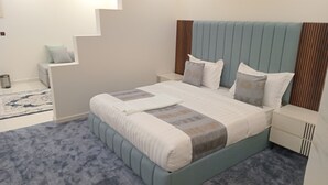 Een moderne slaapkamer met een groot bed, een nachtkastje, een klein zithoekje en een trap.
