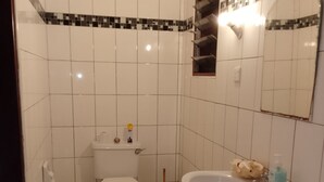 Et badeværelse med hvide fliser, toilet, håndvask, spejl og et håndklædestativ.
