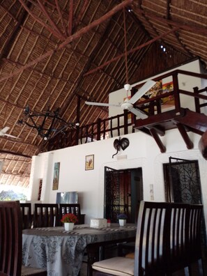 A dining area with a high ceiling, wooden beams, and a table set with a patterned tablecloth. - Artistic Dreamscape 4br Villa Diani Beach, 5 minutes walk to the white beach (Kwale County)