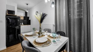 Un comedor moderno con una mesa blanca preparada para cuatro personas, incluyendo platos, cubiertos y vasos.