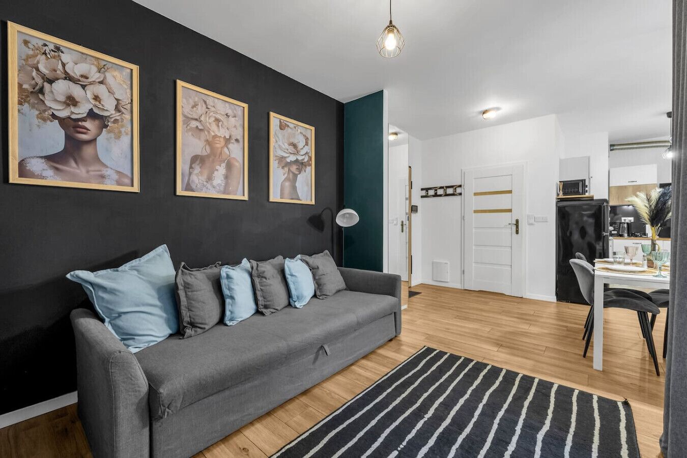 Una sala moderna con un sofá gris, cojines azules y un tapete a rayas negras y blancas. Hay tres cuadros florales enmarcados en la pared.