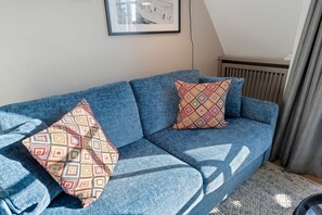 Ein blaues Sofa mit gemusterten Kissen, ein gerahmtes Bild an der Wand und ein Heizkörper.