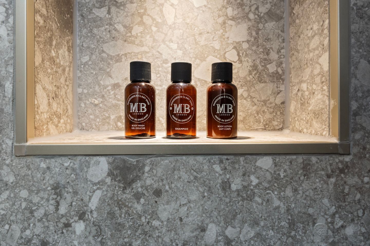 Three bottles of body wash, shampoo, and lotion on a shelf against a textured wall.