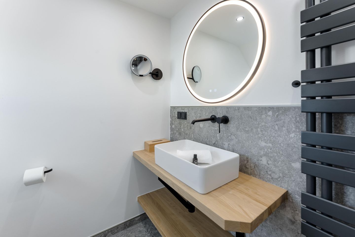 Ein modernes Badezimmer mit einem rechteckigen Waschbecken, einem runden Spiegel mit Beleuchtung und einem Handtuchhalter.