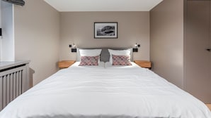 Ein ordentlich eingerichtetes Schlafzimmer mit einem großen Bett, zwei Nachttischen, einem Kopfteil und einem gerahmten Bild an der Wand.