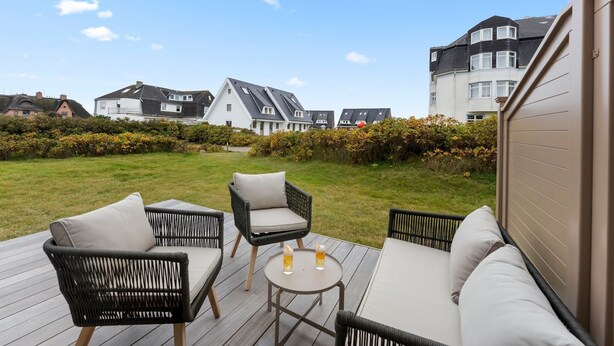 Eine Terrasse mit Gartenmöbeln, ein Rasen und Häuser im Hintergrund.