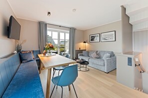 Ein modernes Wohnzimmer mit einem blauen Sofa, einem Esstisch und einem grauen Couchsofa.