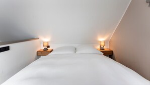 Una camera da letto moderna con soffitto spiovente, un letto grande e due lampade ai comodini.