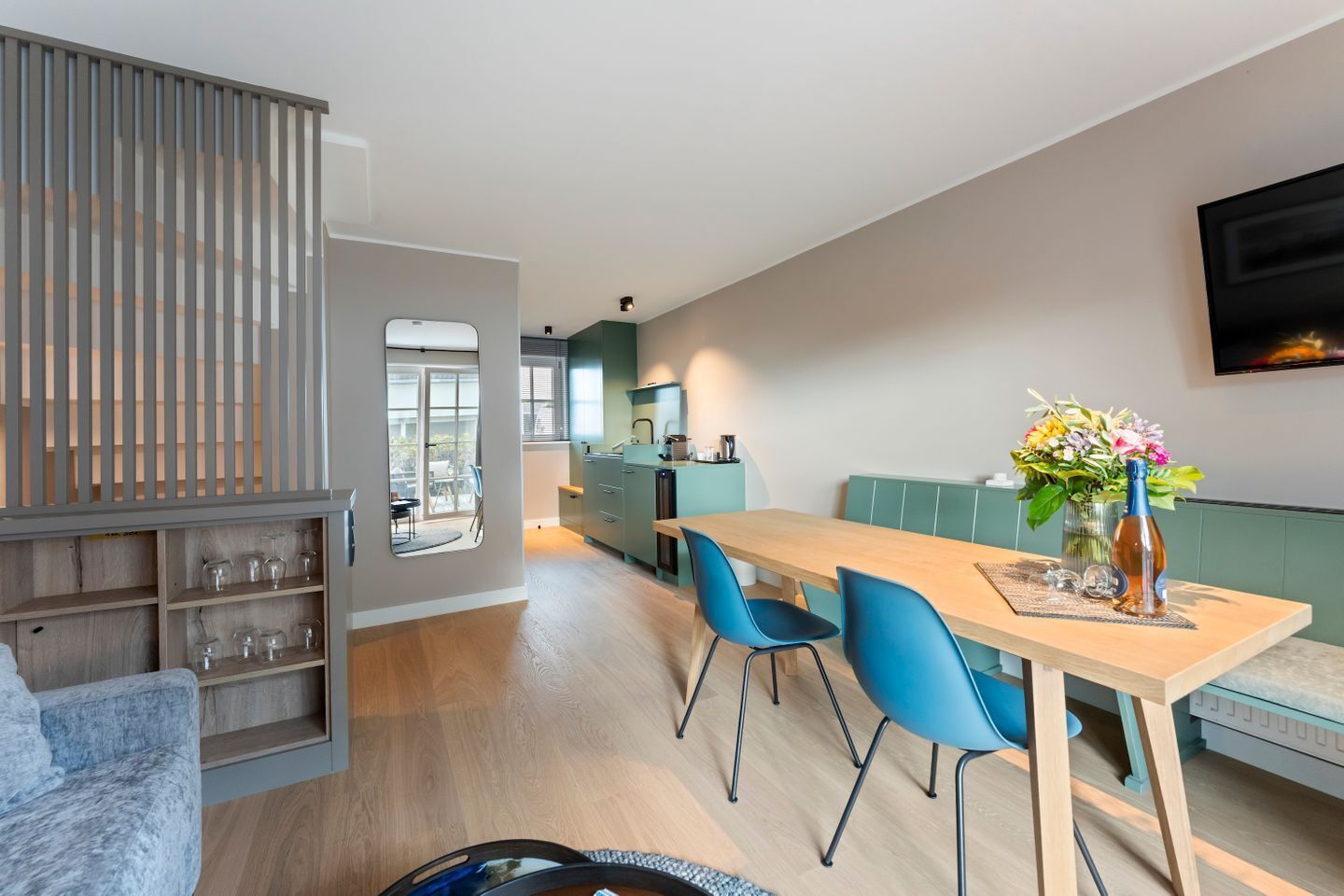 A modern kitchen with a dining area, a sofa, and a TV mounted on the wall.