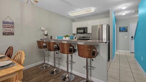 A modern kitchen with white cabinets, stainless steel appliances, and a bar area with wooden stools. - Quiet 2BR Townhome Near Beach, Boardwalk & Hospitals (Myrtle Beach)