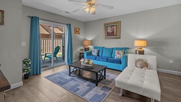A living room with a blue sofa, a white ottoman, a coffee table, two lamps, and a ceiling fan. - Quiet 2BR Townhome Near Beach, Boardwalk & Hospitals (Myrtle Beach)