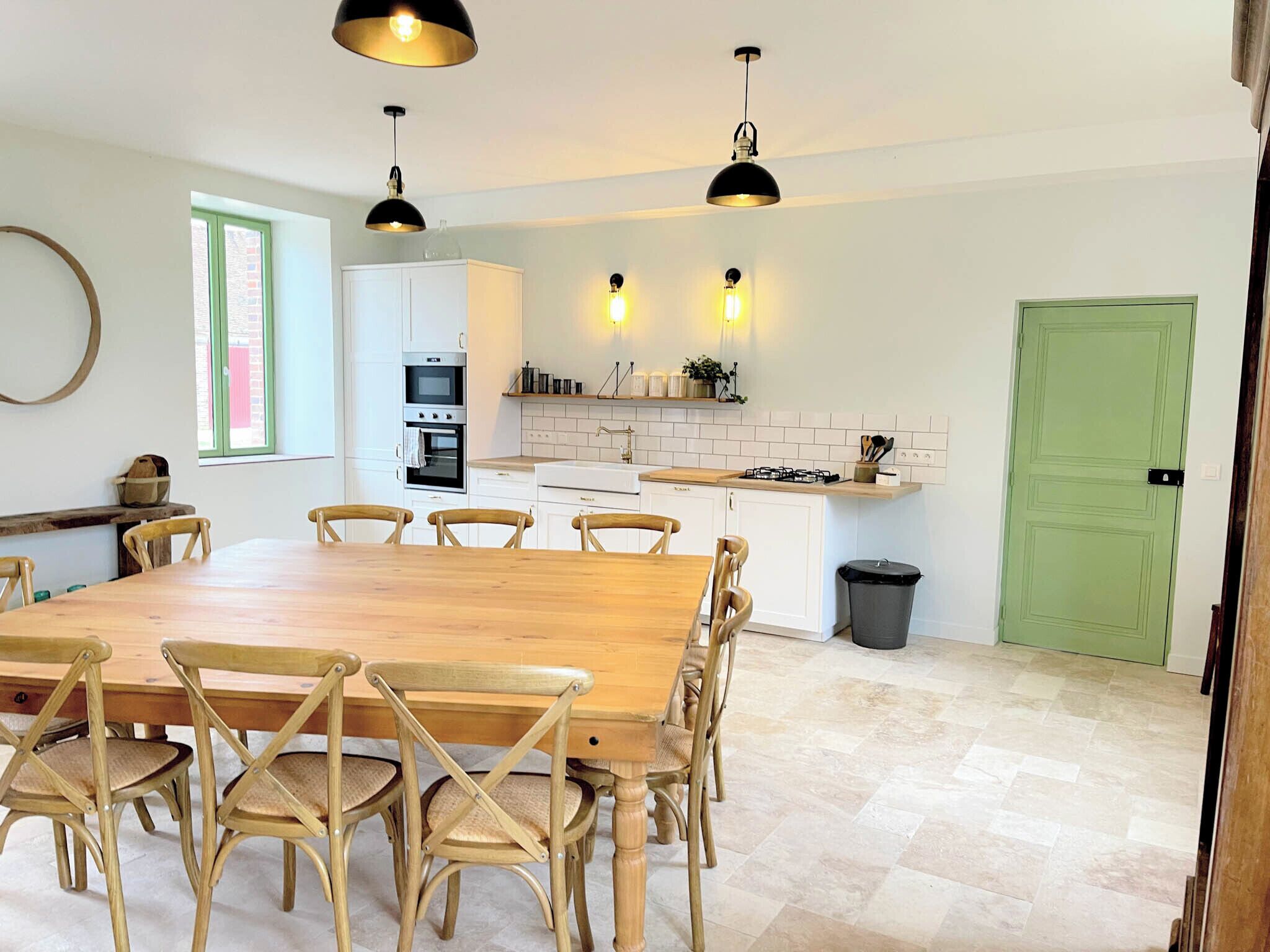 A modern kitchen with white cabinets, a dining table with wooden chairs, and pendant lighting.