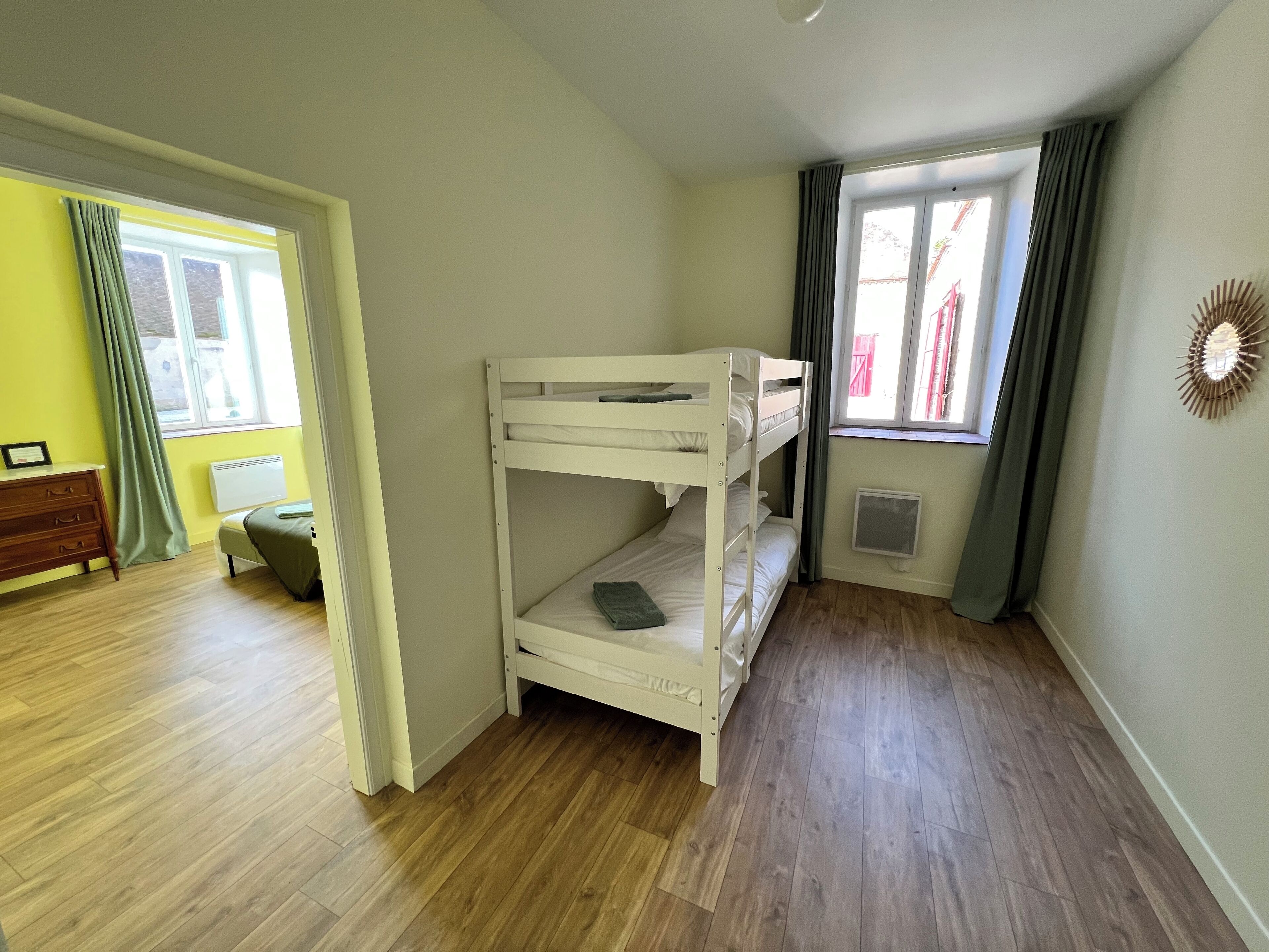 Ein Schlafraum mit Etagenbetten, Holzboden, Kommode und einem Fenster mit Vorhängen.