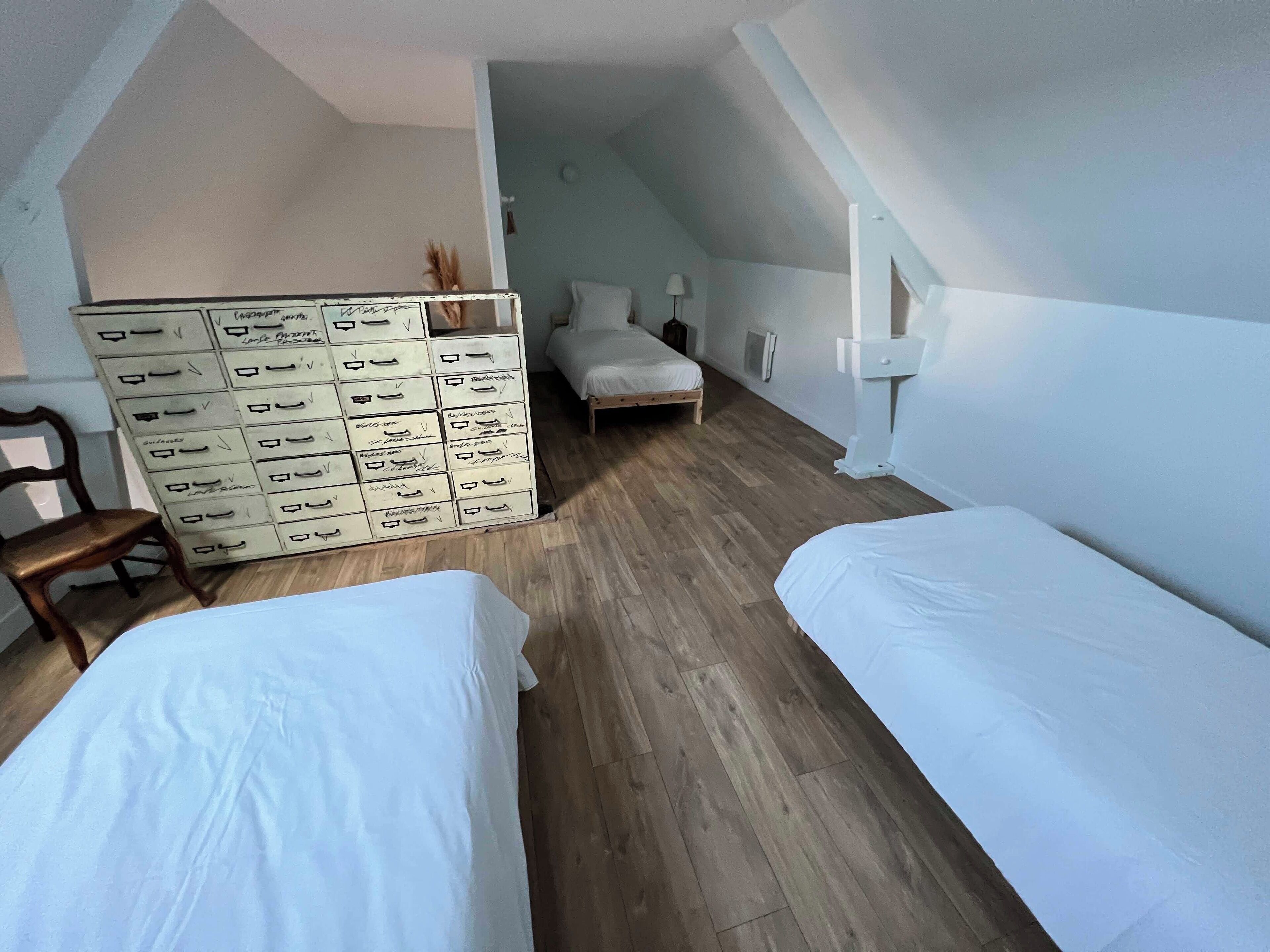Une chambre avec deux lits, une commode avec des tiroirs, une chaise et une lampe.