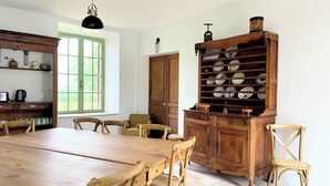 Un coin repas avec une table et des chaises en bois, un buffet rempli de vaisselle et une fenêtre avec des volets verts.