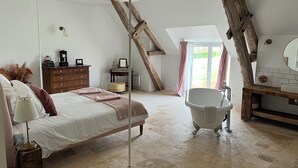 Une chambre à coucher avec un grand lit, une commode en bois, une coiffeuse avec un miroir et une baignoire sur pieds.