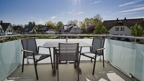 A balcony with a table and chairs, a glass railing, and houses in the background. - Beachfront apartment with balcony, use of swimming pool and sauna - Rex Rugia H-1010 - (Mönchgut)