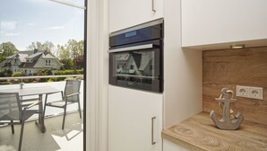 A modern kitchen with a built-in oven, a wooden accent wall, and a view of a residential area. - Beachfront apartment with balcony, use of swimming pool and sauna - Rex Rugia H-1010 - (Mönchgut)