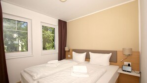 Ein Hotelzimmer mit einem Bett, zwei Nachttischlampen, einem Fernseher und einem Fenster mit Vorhängen.