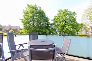 Ein Balkon mit rundem Tisch und zwei Stühlen, umgeben von einem Glasgeländer.