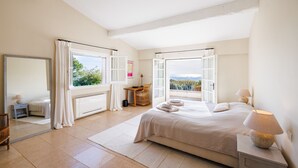 A spacious bedroom with a large bed, a desk, and a view of the outdoors. - Mas Bellevue – Heated Pool & Exceptional Sea View (Saint Paul de Vence)