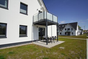 A modern two-story house with a balcony, a patio with outdoor furniture, and a well-maintained lawn. - Beachfront apartment with terrace, use of swimming pool and sauna - Rex Rugia H-1010 - (Mönchgut)