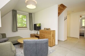 A modern living room with a sofa, a coffee table, a wooden cabinet, and a television. - Beachfront apartment with balcony, use of swimming pool and sauna - Rex Rugia H-1010 - (Mönchgut)