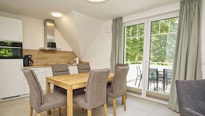 Een moderne keuken met een houten tafel en stoelen, een inbouwoven en een grote schuifpui naar een buitenruimte.