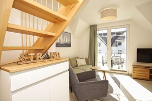 Ein modernes Wohnzimmer mit einer Holztreppe, einem Sofa, einem Sessel und einem Fernseher.