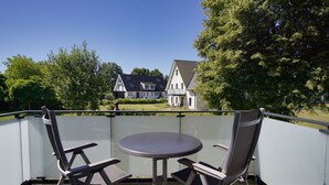 Un balcon avec deux chaises et une table, d’où l’on peut admirer une maison et des arbres.