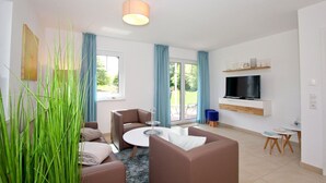 A modern living room with a sofa, a coffee table, a TV mounted on the wall, and a dining area with a small table and chairs. - Beachfront apartment with terrace, use of swimming pool and sauna - Rex Rugia H-1010 - (Mönchgut)