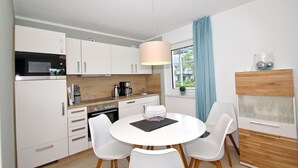 A modern kitchen with white cabinets, a round dining table, and a pendant light. - Beachfront apartment with terrace, use of swimming pool and sauna - Rex Rugia H-1010 - (Mönchgut)