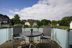 Eine Terrass mit rundem Tisch, zwei Stühlen, einem Blumentopf und Blick auf Häuser im Hintergrund.