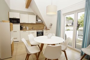 A modern kitchen with white cabinets, a dining table with chairs, and a view through the glass door. - Beachfront apartment with balcony, use of swimming pool and sauna - Rex Rugia H-1010 - (Mönchgut)