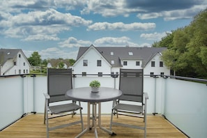 A balcony with a round table and two chairs, a small potted plant, and a view of houses in the background. - Beachfront apartment with balcony, use of swimming pool and sauna - Rex Rugia H-1010 - (Mönchgut)