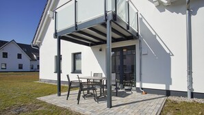 Een modern gebouw met een overdekte patio, een tafel met stoelen en een glazen toegang.
