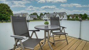 Um terraço ao ar livre com uma mesa redonda e duas cadeiras, uma pequena planta em vaso e vista para casas ao fundo.