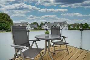 Eine Terrasse im Freien mit einem runden Tisch, zwei Stühlen, einem kleinen Topfpflanzen und Blick auf Häuser im Hintergrund.