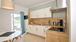 Cozinha moderna com armários brancos, bancada de madeira, pia, cafeteira e área de jantar com mesa e cadeiras.