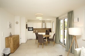 A modern kitchen with white cabinets, a dining area with a wooden table and chairs, and a large window with curtains. - Beachfront apartment with terrace, use of swimming pool and sauna - Rex Rugia H-1010 - (Mönchgut)