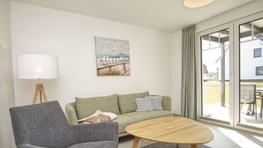 A modern living room with a grey armchair, a green sofa, a wooden coffee table, a floor lamp, and a painting of seagulls. - Beachfront apartment with terrace, use of swimming pool and sauna - Rex Rugia H-1010 - (Mönchgut)
