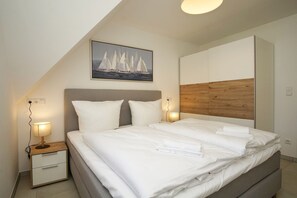 Ein modernes Schlafzimmer mit einem großen Bett, zwei Nachttischen mit Lampen, einem hölzernen Kopfteil und einem Gemälde eines Segelboots an der Wand.