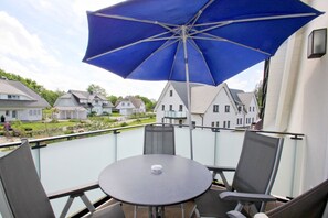 Ein Balkon mit Tisch und Stühlen, einem blauen Sonnenschirm und Blick auf Häuser im Hintergrund.