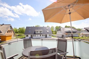 A balcony with a table and chairs, a large umbrella, and houses in the background. - Beachfront apartment with balcony, use of swimming pool and sauna - Rex Rugia H-1010 - (Mönchgut)