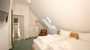 Ein Hotelzimmer mit Bett, Schreibtisch, Stuhl, Kleiderschrank und einem Dachfenster.