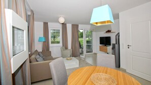Ein modernes Wohnzimmer mit einer Couch, Sesseln, einem Couchtisch, einem Fernseher und einer Küchenzeile mit Kühlschrank und Mikrowelle.